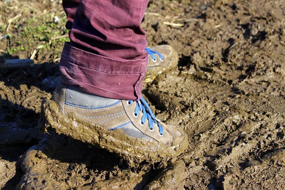 man wearing hiking shoes walking in wet mud trail