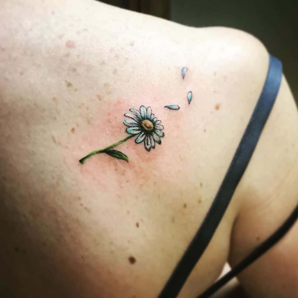 Shoulder blade tattoo tiny color white and yellow daisy with stem and petals blowing in the wind