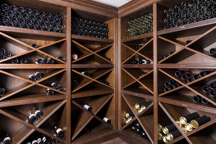 Corner wine cellar with diagonal wooden shelves holding neatly arranged wine bottles.